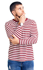 Sticker - Young handsome man wearing striped sweater with hand on chin thinking about question, pensive expression. smiling with thoughtful face. doubt concept.