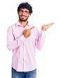 © Krakenimages.com - Handsome young man with curly hair and bear wearing business clothes amazed and smiling to the camera while presenting with hand and pointing with finger.