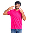 © Krakenimages.com - Handsome young man with curly hair and bear wearing casual pink tshirt smiling cheerful showing and pointing with fingers teeth and mouth. dental health concept.