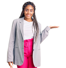 Wall Mural - Young african american woman with braids wearing business clothes smiling cheerful presenting and pointing with palm of hand looking at the camera.