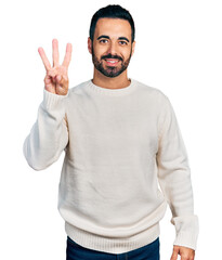 Canvas Print - Young hispanic man with beard wearing casual white sweater showing and pointing up with fingers number three while smiling confident and happy.