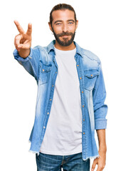 Wall Mural - Attractive man with long hair and beard wearing casual denim jacket smiling looking to the camera showing fingers doing victory sign. number two.