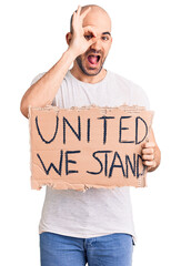 Poster - Young handsome man holding united we stand banner smiling happy doing ok sign with hand on eye looking through fingers