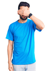 Wall Mural - Young handsome man with beard wearing casual t-shirt covering eyes with hand, looking serious and sad. sightless, hiding and rejection concept