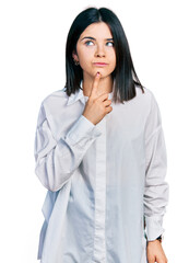 Poster - Young brunette woman with blue eyes wearing oversize white shirt thinking concentrated about doubt with finger on chin and looking up wondering