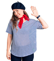 Poster - Young beautiful blonde woman wearing french beret and striped t-shirt waiving saying hello happy and smiling, friendly welcome gesture