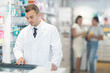 © JackF - Young male pharmacist in uniform looking for medicine in pharmacy using computer