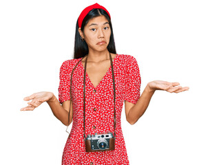 Sticker - Beautiful young asian woman wearing dress and vintage camera clueless and confused expression with arms and hands raised. doubt concept.