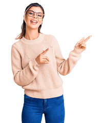 Wall Mural - Young beautiful woman wearing casual winter sweater and glasses smiling and looking at the camera pointing with two hands and fingers to the side.