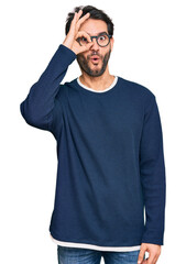 Sticker - Young hispanic man wearing casual clothes and glasses doing ok gesture shocked with surprised face, eye looking through fingers. unbelieving expression.