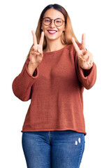 Wall Mural - Beautiful young woman wearing casual clothes and glasses smiling looking to the camera showing fingers doing victory sign. number two.