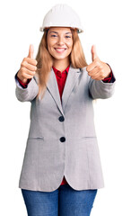 Poster - Beautiful young woman wearing architect hardhat approving doing positive gesture with hand, thumbs up smiling and happy for success. winner gesture.