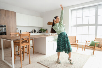 Poster - Beautiful young happy woman in headphones listening music and dancing at kitchen