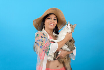 Woman in casual beachwear with positive attitude, hugging her cat. Blue background.