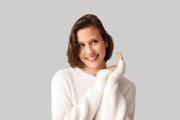 Happy young woman in stylish white sweater on grey background