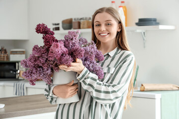 Poster - Young woman holding vase of lilacs near counter in kitchen