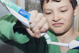 Fototapeta Maki - Boy in green bathrobe with an electric toothbrush squeezing toothpaste.