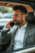 Well-dressed businessman in a stylish suit is seen having important business discussion on his phone while commuting in the back seat of luxurious car. Man in suit talking on phone in back seat of car