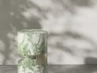Round marble green podium in dappled sunlight, tree leaf shadow on gray wall for modern, luxury fashion, beauty, cosmetic, skincare, body care, product background 3D
