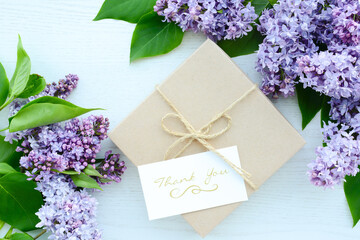 Wall Mural - Gift box and card with text Thank you and Lilac flowers on white wooden background, flat lay, top view. Beautiful floral background for greeting card for Birthday, Mother's Day, Thanksgiving day