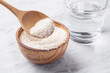 Psyllium husk in spoon and wood bowl with glass of water, fiber food for diet on white marble table