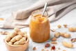 Peanut butter in jar with spoon and peanuts in shell in wood bowl on marble table