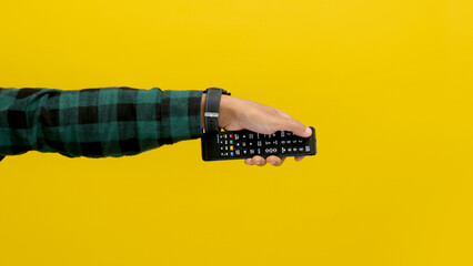 hand holding a black tv remote, isolated on a yellow background