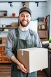 Smiling Delivery Man in Green Apron Holding a Package in a Modern Kitchen