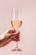 Hand Holding a Glass of Rosé Wine Against a Soft Pink Background