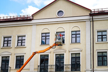 Man on cradle washing glass and clean facade wall of historic building in downtown. Facade cleaning service, worker in lift bucket wash windows. Labor washing window and facade of historic building.