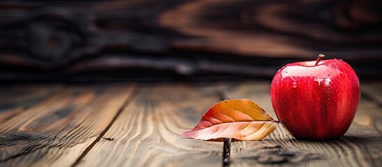 Wall Mural - A red apple is seen in the foreground placed on a rustic wooden surface surrounded by dry leaves The composition creates a warm and natural ambiance The image incorporates copy space