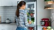 © Irina Ukrainets - Young woman at home browsing through a healthy stocked fridge. Casual lifestyle. Modern kitchen setting. Daily routine. AI