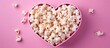 © HN Works - A close up shot of a wooden heart shaped box of popcorn on a pink background viewed from the top with copy space