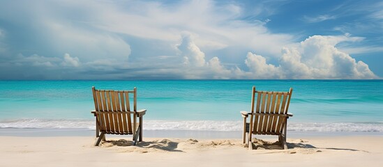 Poster - Two wooden chairs are positioned on the tropical beach with a scenic backdrop of a turquoise sea and cloudy sky. Creative banner. Copyspace image