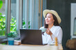 Portrait image of a young woman with hat drinking coffee while working on laptop computer  in cafe