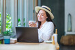 Portrait image of a young woman with hat drinking coffee while working on laptop computer in cafe