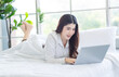 © Bangkok Click Studio - Asian beautiful woman girl in her bedroom smiling relaxed searching, playing social on her laptop on white bed in the morning after waking up at home, concept chat with someone online.