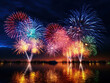 Colorful fireworks exploding over calm waterfront at night with reflections on the water creating dazzling effect