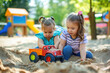 Two girls having fun playing together with toy truck in sand pit
