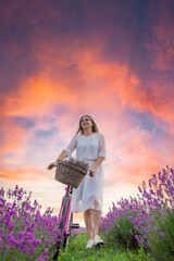 Wall Mural - a woman in a white dress walks through a lavender field with a bicycle.