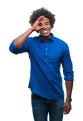 Canvas Print - Afro american man over isolated background doing ok gesture with hand smiling, eye looking through fingers with happy face.