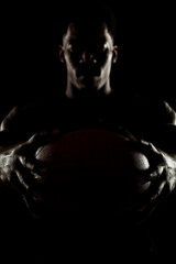 Wall Mural - Basketball player holding a ball against black background. Serious concentrated african american man. Muscular person sidelit silhouette.