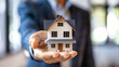 © Anoo - A man holding a small model house in his hands, representing the concepts of real estate, mortgages, and property sales