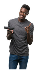 Poster - Young african american man holding a gun very happy pointing with hand and finger to the side