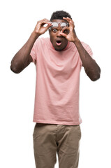 Poster - Young african american man wearing pink t-shirt doing ok gesture shocked with surprised face, eye looking through fingers. Unbelieving expression.