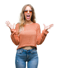 Poster - Beautiful young blonde woman wearing sunglasses over isolated background crazy and mad shouting and yelling with aggressive expression and arms raised. Frustration concept.