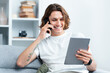 Young Man Enjoying Conversation On Phone While Holding Tablet, Sitting In A Modern Living Room, Exuding Happiness And Casual Lifestyle. Perfect For Telecommunication And Technology Themes.