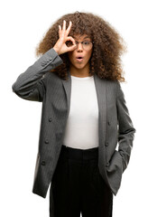 Poster - African american business woman wearing glasses doing ok gesture shocked with surprised face, eye looking through fingers. Unbelieving expression.