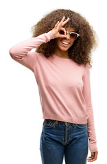 Wall Mural - African american woman wearing pink sunglasses doing ok gesture with hand smiling, eye looking through fingers with happy face.