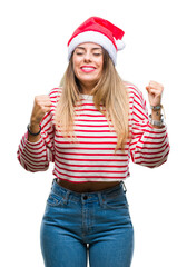 Wall Mural - Young beautiful woman wearing christmas hat over isolated background very happy and excited doing winner gesture with arms raised, smiling and screaming for success. Celebration concept.